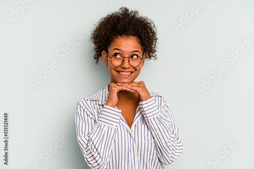 Young Brazilian woman isolated on blue background keeps hands under chin, is looking happily aside.