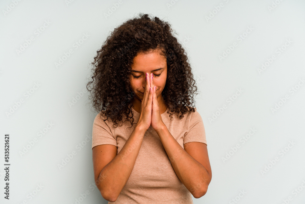 Young Brazilian woman isolated on blue background praying, showing devotion, religious person looking for divine inspiration. Young Brazilian woman isolated on blue background praying, showing devotion, religious person looking for divine inspiration.