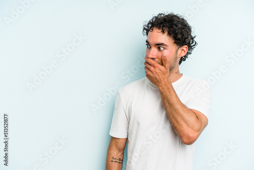 Young caucasian man isolated on blue background thoughtful looking to a copy space covering mouth with hand.