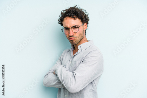 Young caucasian man isolated on blue background frowning face in displeasure, keeps arms folded. © Asier