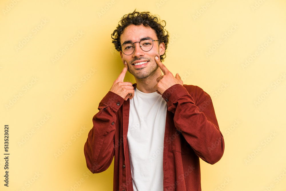 Young caucasian man isolated on yellow background smiles, pointing fingers at mouth.