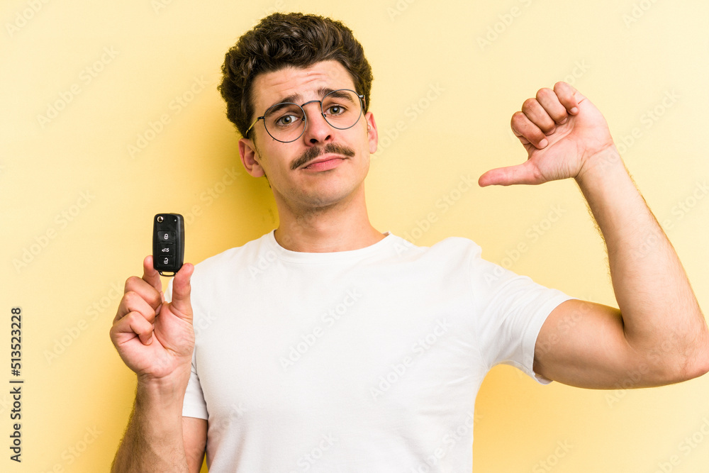 Young caucasian man holding car keys isolated on yellow background feels proud and self confident, example to follow. Young caucasian man holding car keys isolated on yellow background feels proud and self confident, example to follow.