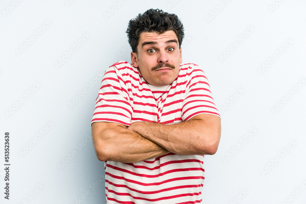 Young caucasian man isolated on blue background shrugs shoulders and open eyes confused. Young caucasian man isolated on blue background shrugs shoulders and open eyes confused.