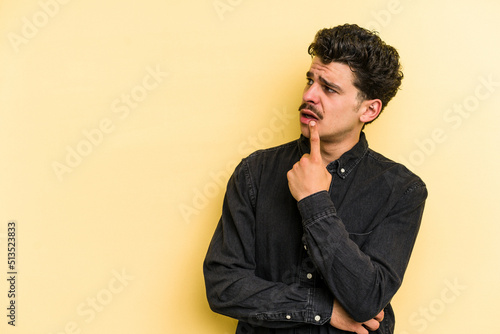 Young caucasian man isolated on yellow background looking sideways with doubtful and skeptical expression.