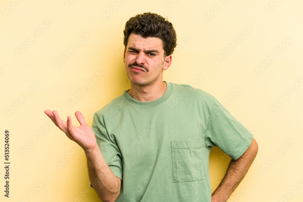 Young caucasian man isolated on yellow background doubting and shrugging shoulders in questioning gesture. Young caucasian man isolated on yellow background doubting and shrugging shoulders in questioning gesture.