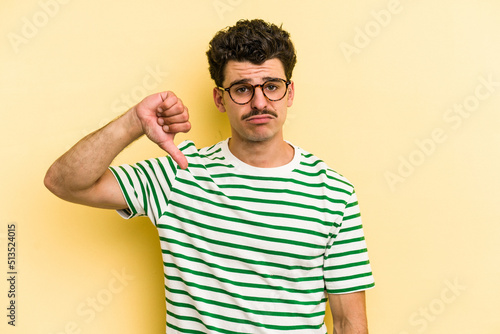 Young caucasian man isolated on yellow background showing a dislike gesture, thumbs down. Disagreement concept.