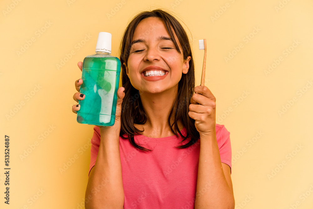 Young hispanic woman holding mouthwash isolated on yellow background Young hispanic woman holding mouthwash isolated on yellow background