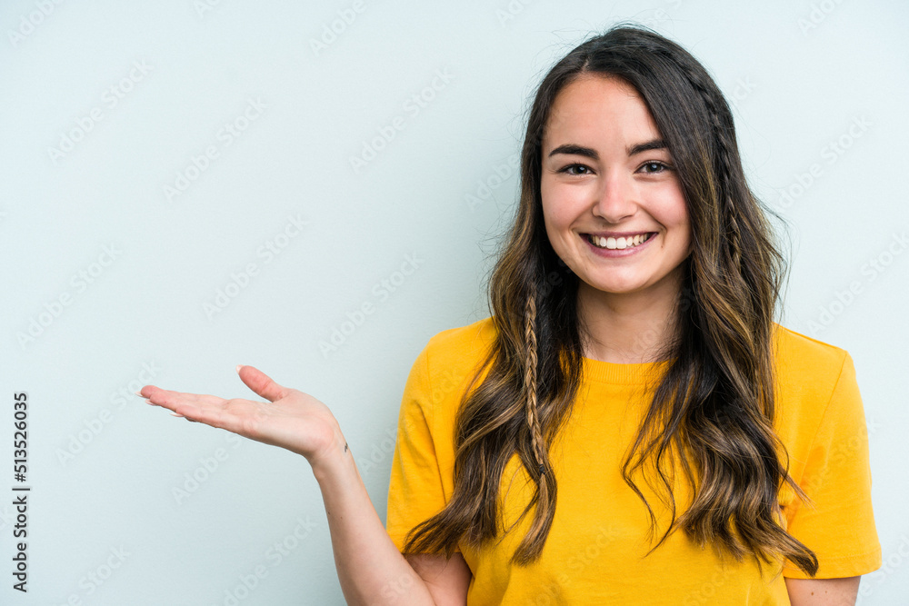 Young caucasian woman isolated on blue background showing a copy space on a palm and holding another hand on waist. Young caucasian woman isolated on blue background showing a copy space on a palm and holding another hand on waist.