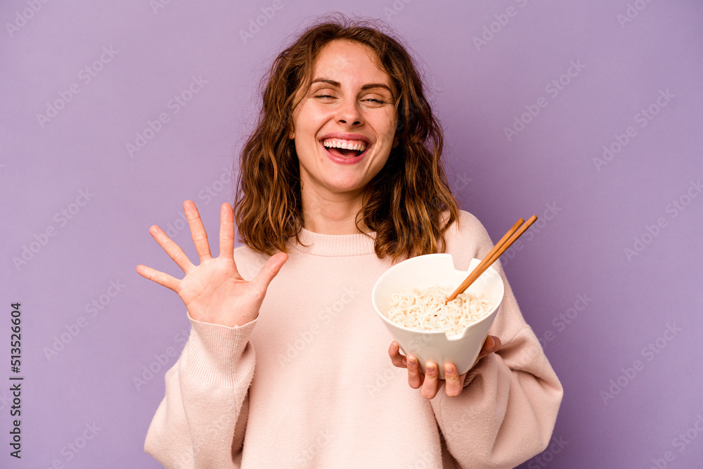 Young caucasian woman eating noodles isolated on purple background smiling cheerful showing number five with fingers. Young caucasian woman eating noodles isolated on purple background smiling cheerful showing number five with fingers.