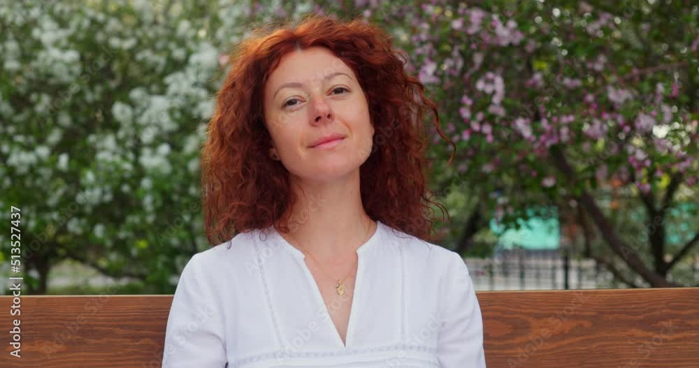 A beautiful red-haired woman sits on a bench in a blooming garden and reads a book. A beautiful red-haired woman sits on a bench in a blooming garden and reads a book.