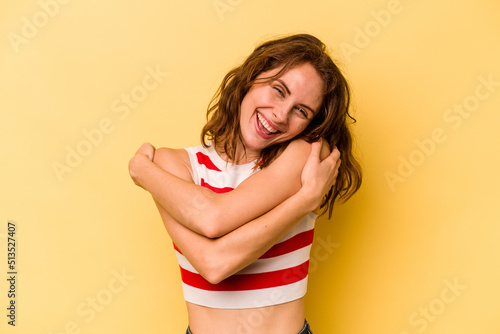 Young caucasian woman isolated on yellow background hugs, smiling carefree and happy. photo