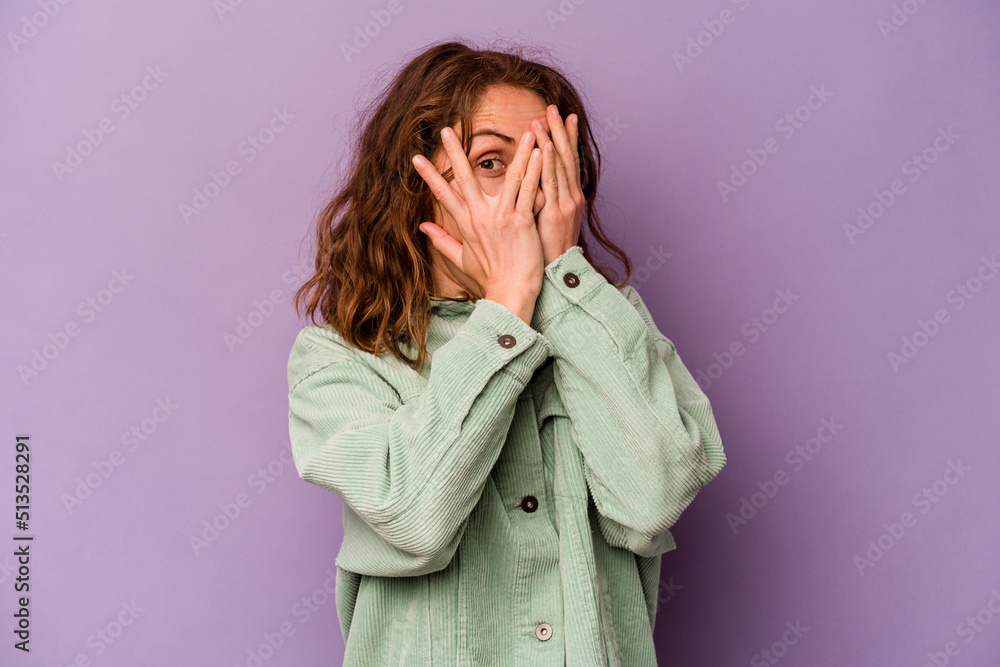 Young caucasian woman isolated on purple background blink through fingers frightened and nervous. Young caucasian woman isolated on purple background blink through fingers frightened and nervous.