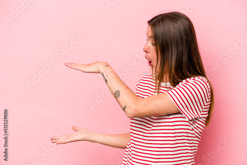 Young caucasian pregnant woman isolated on white background shocked and amazed holding a copy space between hands. © Asier