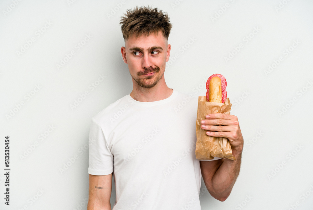 Young caucasian man holding a sandwich isolated on white background confused, feels doubtful and unsure. Young caucasian man holding a sandwich isolated on white background confused, feels doubtful and unsure.