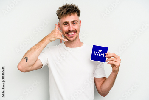 Young caucasian man holding wifi placard isolated on white background showing a mobile phone call gesture with fingers.