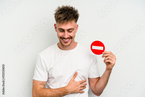 Young caucasian man holding a forbidden sign isolated on white background laughing and having fun.