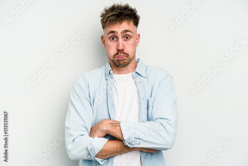 Young caucasian man isolated on white background blows cheeks, has tired expression. Facial expression concept.