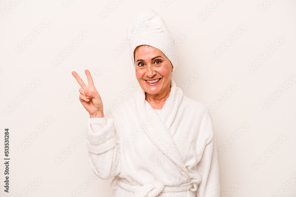 Middle age caucasian woman wearing a bathrobe isolated on white background joyful and carefree showing a peace symbol with fingers. Middle age caucasian woman wearing a bathrobe isolated on white background joyful and carefree showing a peace symbol with fingers.