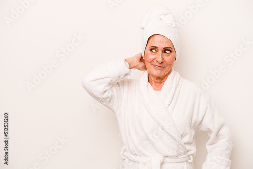 Middle age caucasian woman wearing a bathrobe isolated on white background touching back of head, thinking and making a choice.