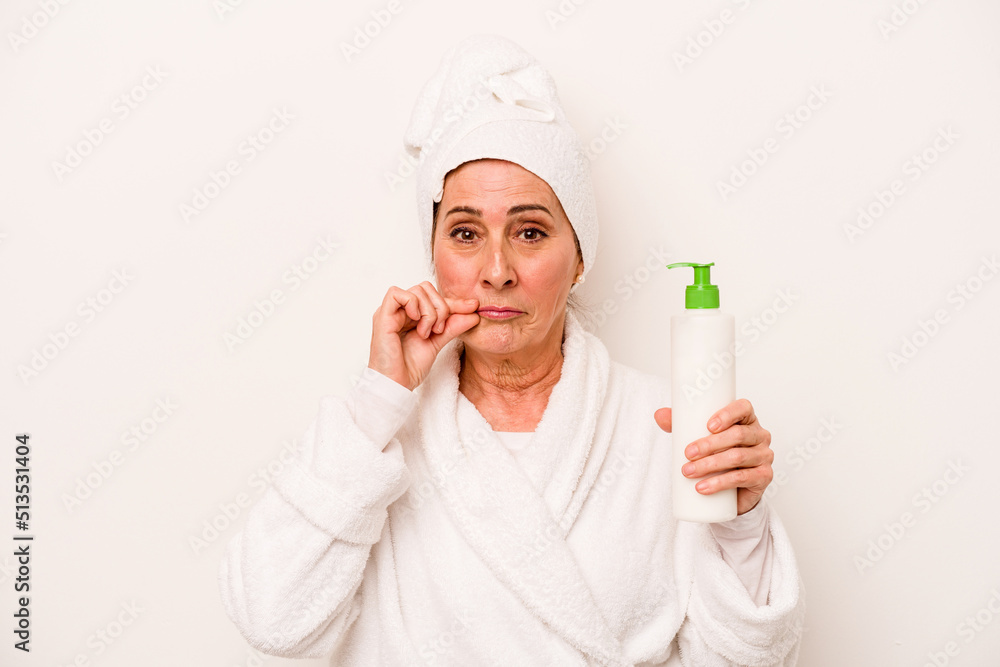 Middle age caucasian woman wearing a bathrobe holding body cream isolated on white background with fingers on lips keeping a secret. Middle age caucasian woman wearing a bathrobe holding body cream isolated on white background with fingers on lips keeping a secret.