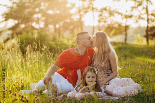 Young beautiful family with a little daughter hug, kiss and walk in nature at sunset. Photo of a family with a small child in nature.