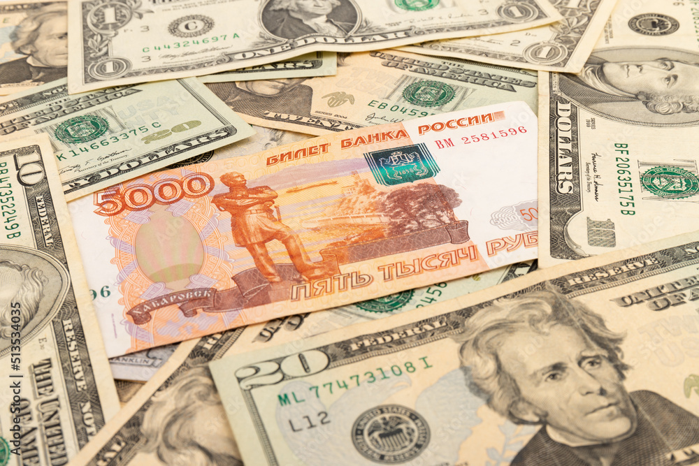 Russian national currency on top of US dollar banknote, top view of mixed rouble banknotes. Russian and American paper money. Rubles and US dollars exchange rate. Russian national currency on top of US dollar banknote, top view of mixed rouble banknotes. Russian and American paper money. Rubles and US dollars exchange rate.