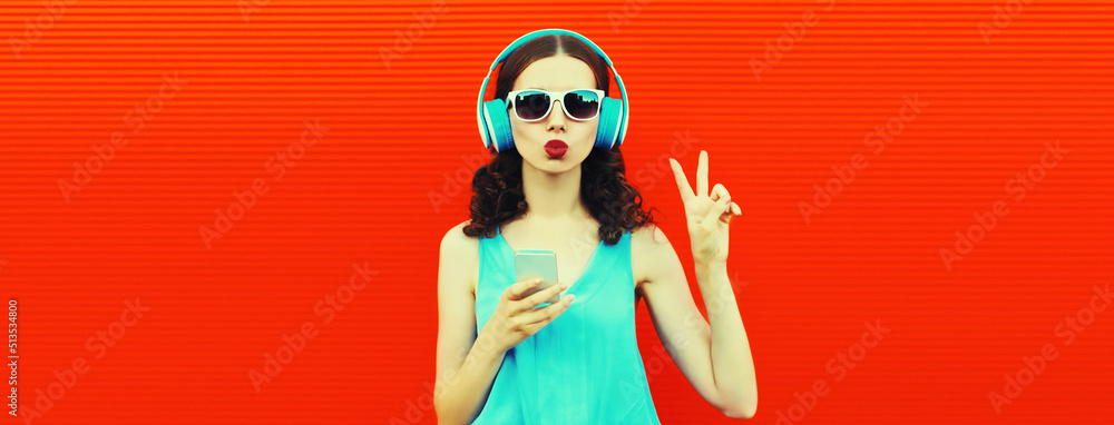 Portrait of young woman in headphones listening to music with smartphone on red background