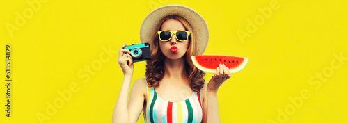 Summer portrait of stylish young woman with film camera and slice of fresh watermelon wearing straw hat posing on yellow background © rohappy