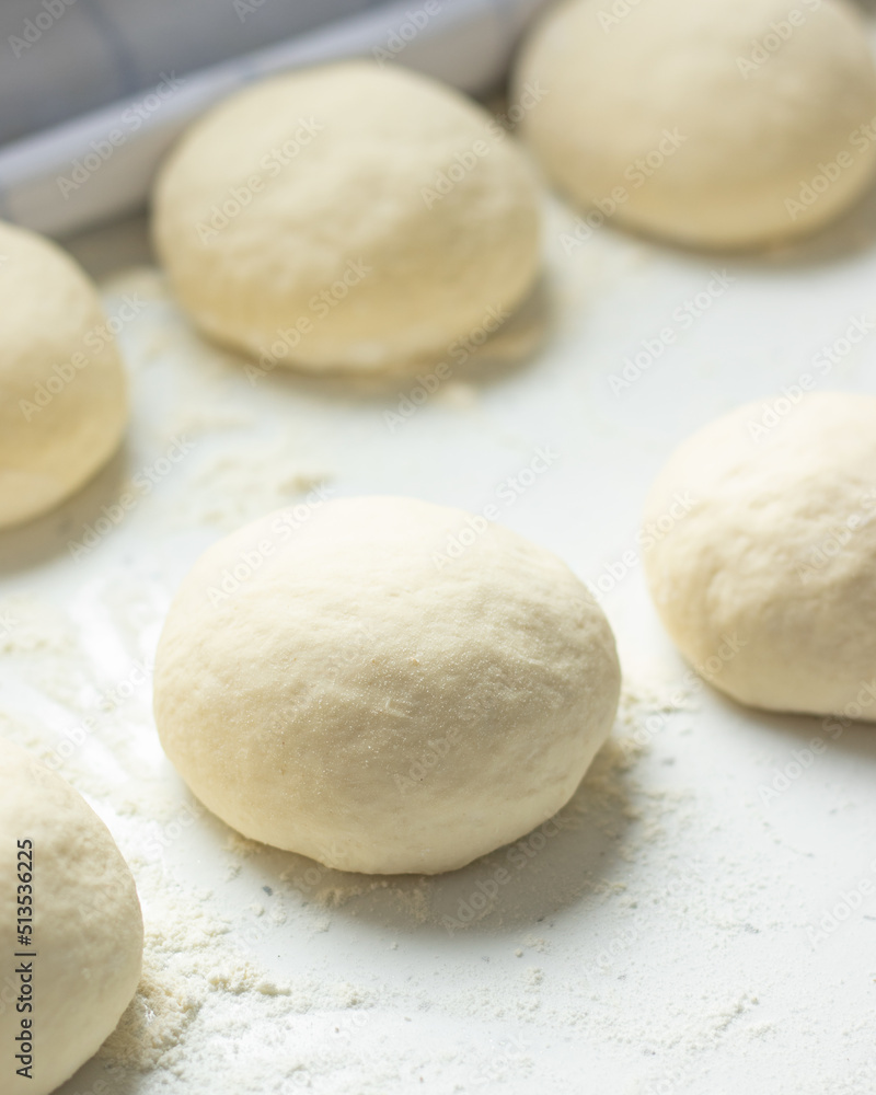 Homemade pizza dough with wheat flour dusted on a white kitchen table. Freshly kneaded bread buns ready to be baked. Vertical shot. A closeup.