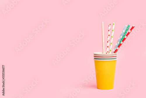 Vasos de cartón de cumpleaños y fiesta de colores con pajitas sobre un fondo rosa liso y aislado. Vista de frente y de cerca. Copy space