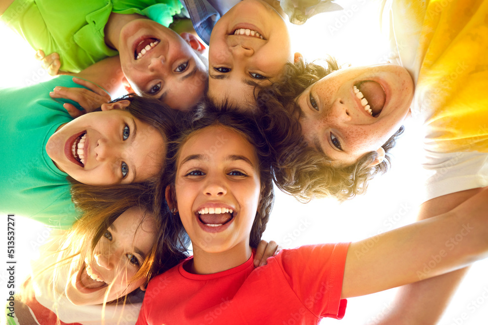 Bunch of cheerful joyful cute little children playing together and having fun. Group portrait of happy kids huddling, looking down at camera and smiling. Low angle, view from below. Friendship concept - obrazy, fototapety, plakaty 