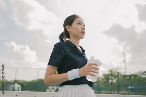Asian young woman tennis player drinking water and taking a break during a practice.