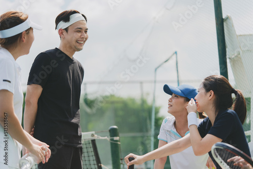 Happy asian young friendship sitting, talking and resting after match on the outside tennis court.