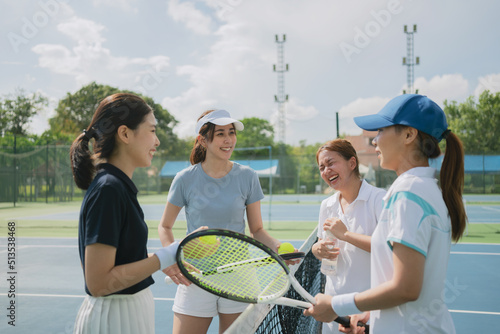 Happy asian young friendship talking and resting after match on the outdoor tennis court on a bright sunny day. © Suradech
