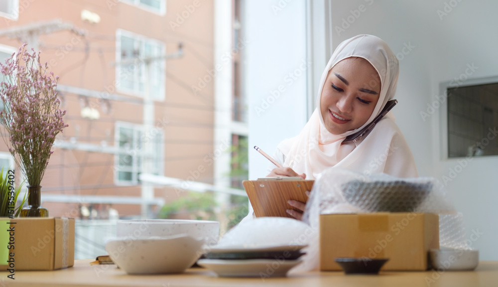 Young muslim woman in hijab confirming orders from customer on mobile phone. Small business owner, Online selling, E-commerce concept. Young muslim woman in hijab confirming orders from customer on mobile phone. Small business owner, Online selling, E-commerce concept.