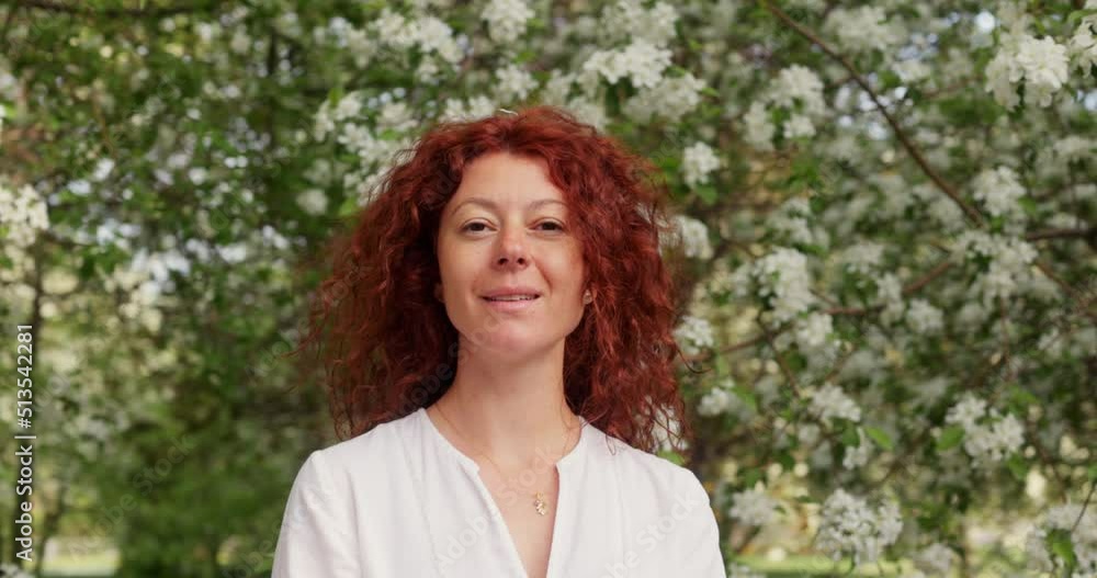 Portrait of a beautiful red-haired woman without makeup on her face in a blooming apple orchard Portrait of a beautiful red-haired woman without makeup on her face in a blooming apple orchard