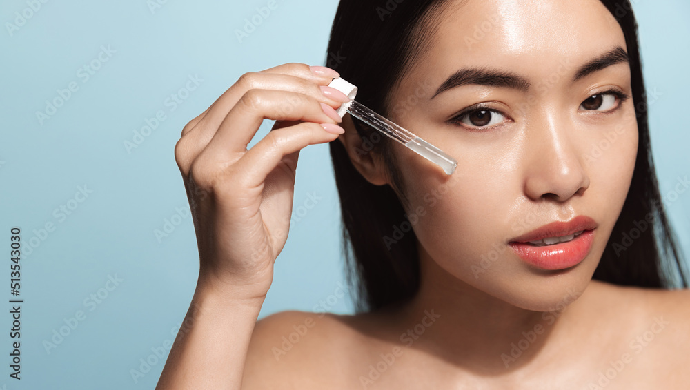 Fototapeta premium Close up of young asian woman with beautiful skin. Female model with fresh and healthy skin looking at camera. Girl with dropper applies serum, collagen and argan oil moisturizer