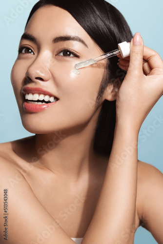 Beauty collagen. Vertical of beautiful asian woman applies C-serum  tea trea argan oil skincare treatment  daily care skin regime  blue background