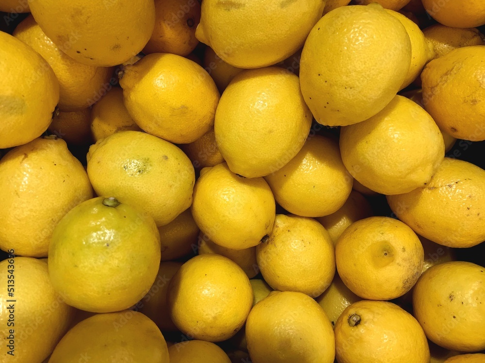 Fresh juicy and sour citrus fruit, macro shot of yellow round lemons. Stock photo of a large box with a bunch of lemons. Refreshing fruit, ingredient for lemonade. For background, design, print