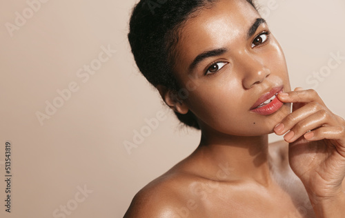 Close up of african american woman with glowing, clean and perfect facial skin, touches her face after daily cream, nourishment mask, brown background