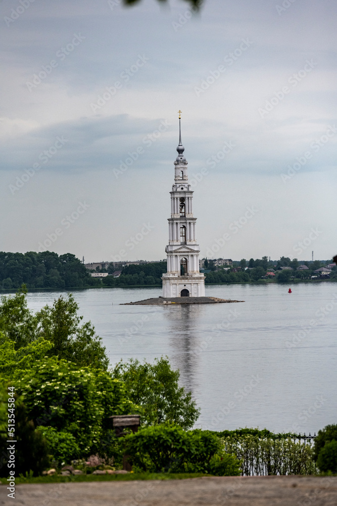 an old white high bell tower in the middle of the river against the background of the forest on a summer day an old white high bell tower in the middle of the river against the background of the forest on a summer day