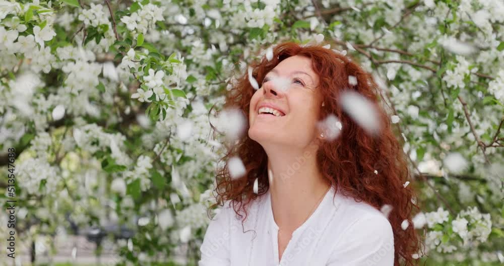 Red-haired woman looking at the camera and smiling in a blooming apple orchard Red-haired woman looking at the camera and smiling in a blooming apple orchard