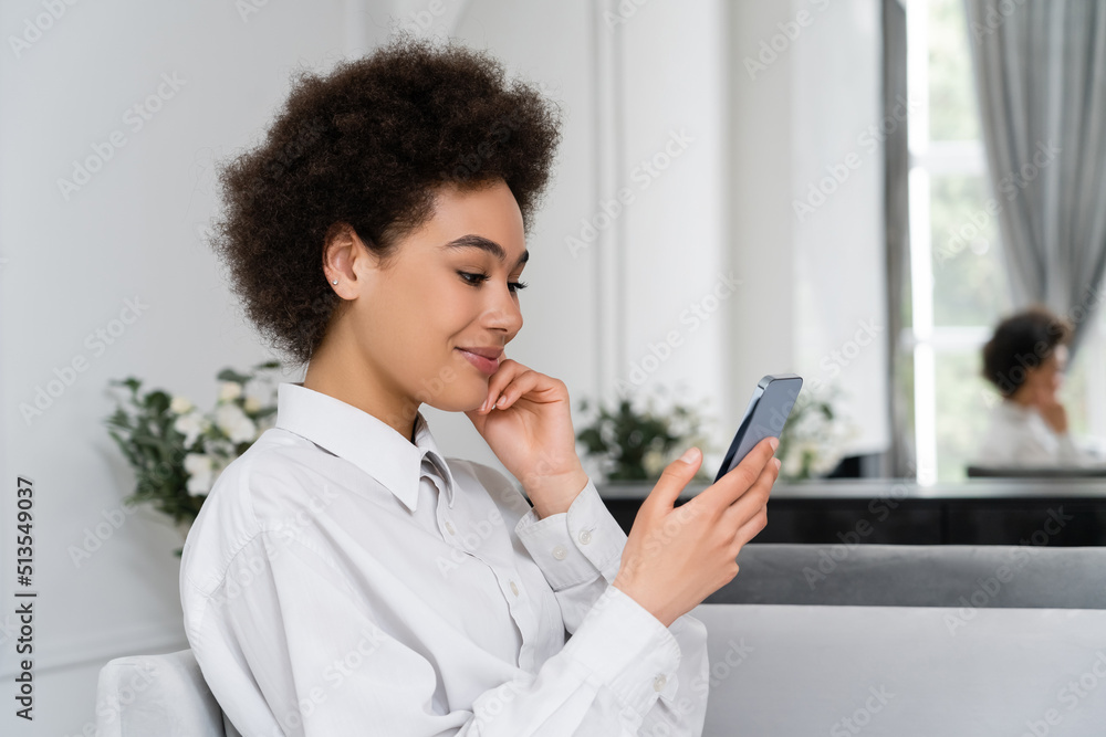 joyful african american woman smiling while using smartphone at home. joyful african american woman smiling while using smartphone at home.