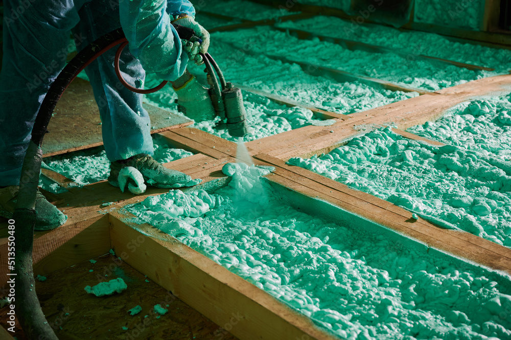 Male builder insulating wooden frame house. Cropped view of man worker spraying polyurethane foam on floor inside of future cottage, using plural component gun. Construction and insulation concept. - obrazy, fototapety, plakaty 