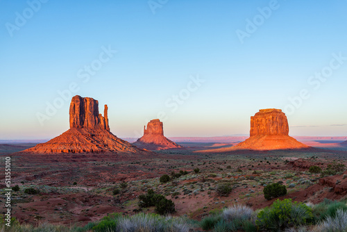Famous view Monument Valley buttes and horizon at vibrant red sunset colorful light in Arizona with orange rocks formations and plans with blue sky photo