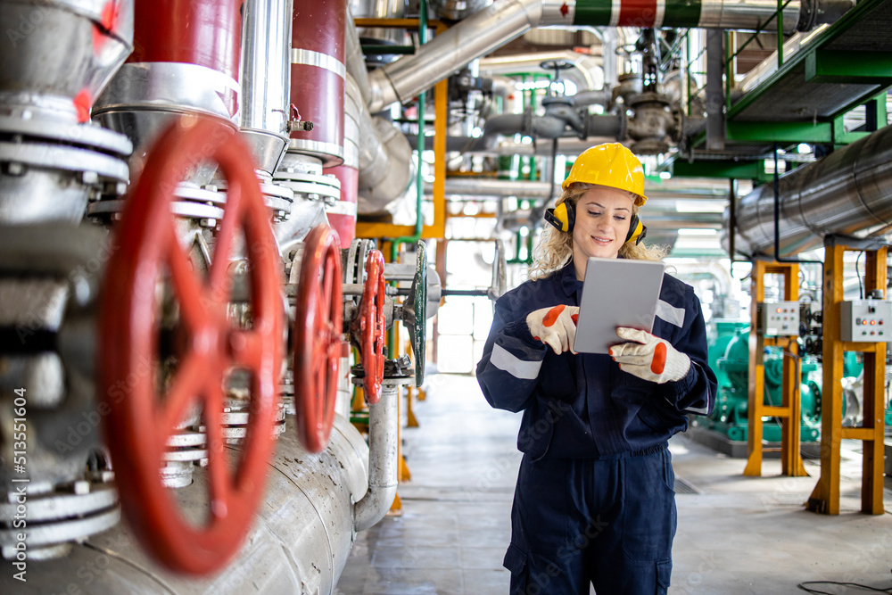 Female factory worker or engineer standing in boiler room of heating plant and looking at tablet computer. Female factory worker or engineer standing in boiler room of heating plant and looking at tablet computer.