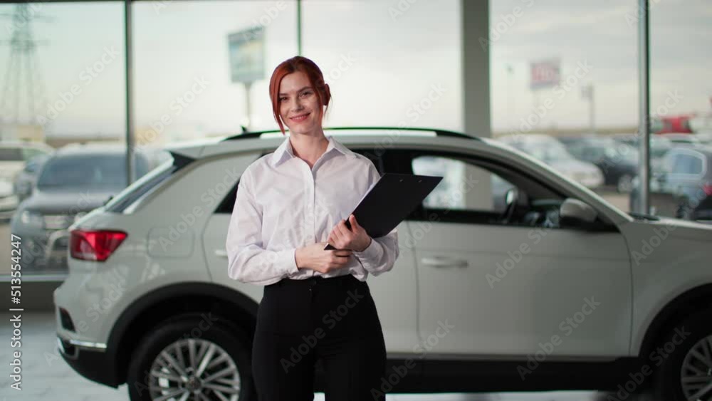 portrait of auto sales female manager holding keys in front of a new car, smiling and looking at camera portrait of auto sales female manager holding keys in front of a new car, smiling and looking at camera