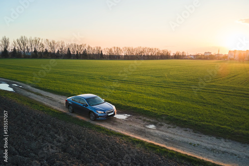 Aerial view of sedan car driving fast on dirt road at sunset. Traveling by vehicle concept