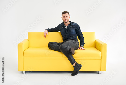 Young trendy man posing sitting on yellow sofa looking to camera