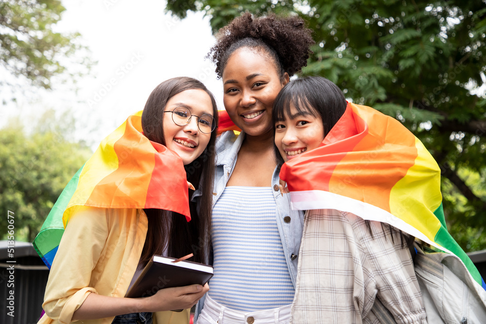Diversity young gay women with Asian gay embrace pride rainbow flag in their backs supporting LGBTQ pride in the park. Independence and polygamy. Supporters of the LGBT community Diversity young gay women with Asian gay embrace pride rainbow flag in their backs supporting LGBTQ pride in the park. Independence and polygamy. Supporters of the LGBT community